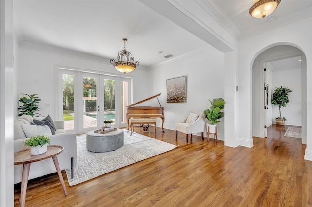 living area with visible vents, light wood-style flooring, arched walkways, french doors, and crown molding