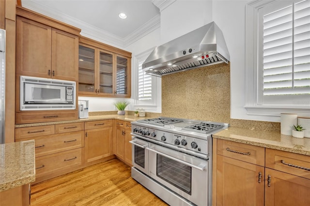 kitchen with light stone counters, stainless steel appliances, wall chimney range hood, and ornamental molding