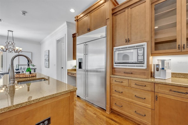 kitchen featuring ornamental molding, a sink, light wood-style floors, built in appliances, and hanging light fixtures