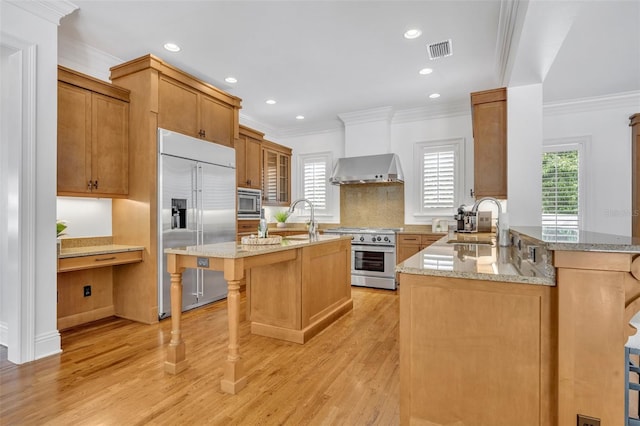 kitchen featuring visible vents, a sink, built in appliances, a kitchen bar, and wall chimney exhaust hood