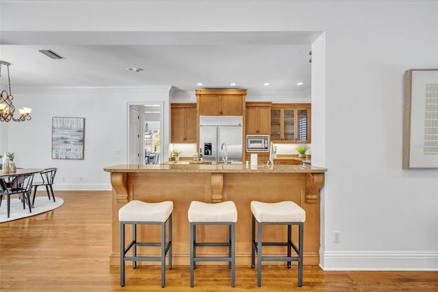 kitchen featuring a kitchen breakfast bar, brown cabinetry, light wood-type flooring, and built in appliances