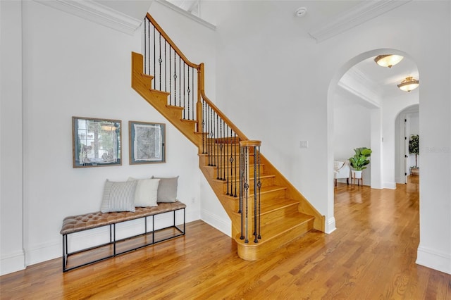 staircase with baseboards, arched walkways, wood finished floors, and crown molding