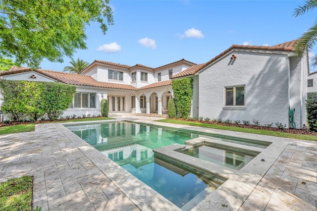 back of house featuring stucco siding, a pool with connected hot tub, and a patio