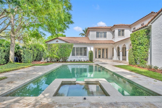 rear view of property featuring a pool with connected hot tub, a tiled roof, stucco siding, french doors, and a patio area