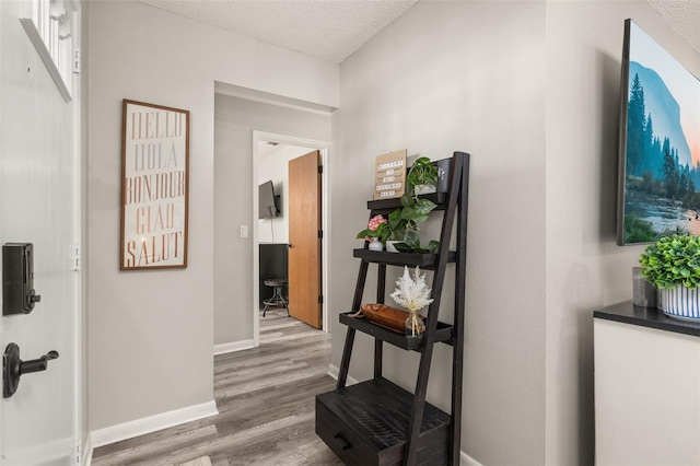 hall with wood finished floors, baseboards, and a textured ceiling