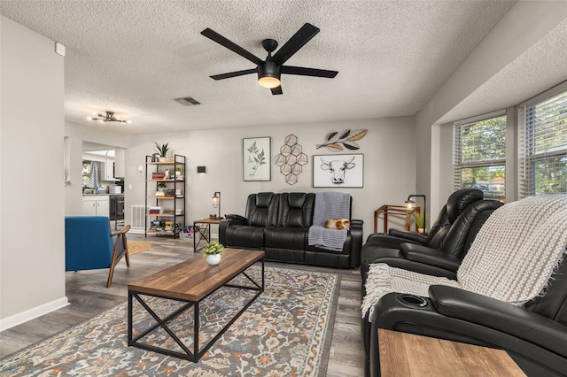 living room featuring visible vents, baseboards, ceiling fan, wood finished floors, and a textured ceiling