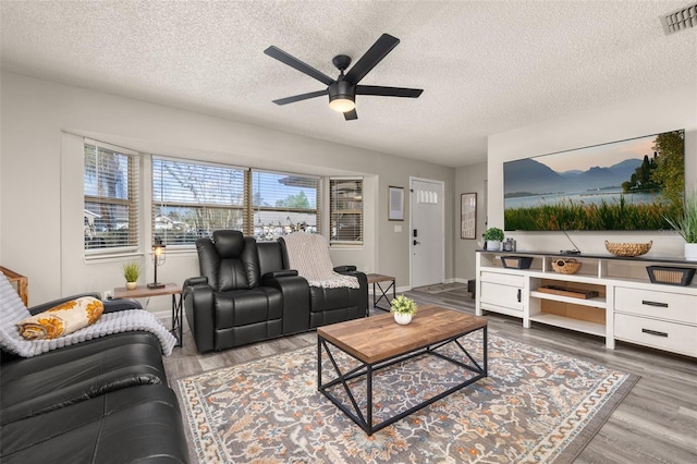 living room featuring a textured ceiling, wood finished floors, visible vents, and ceiling fan