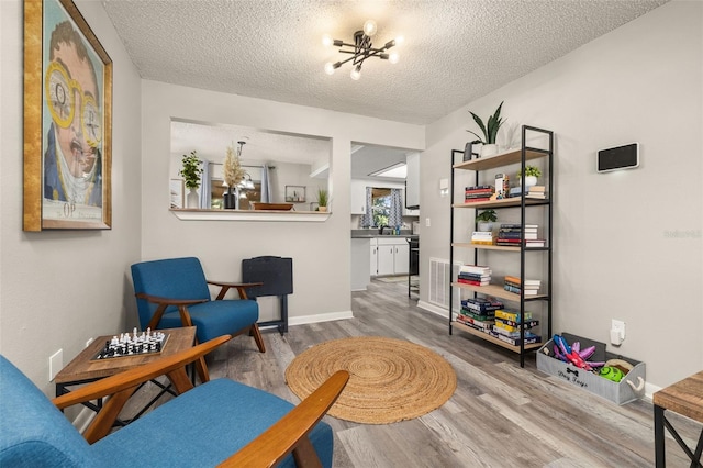 living area featuring baseboards, a notable chandelier, wood finished floors, and a textured ceiling