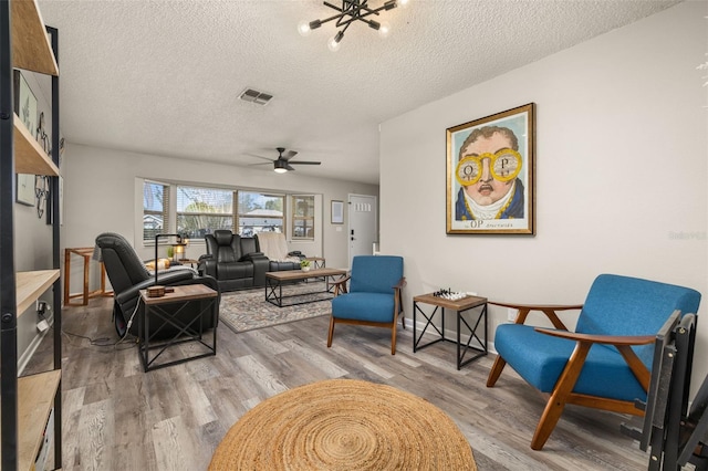 living room featuring a textured ceiling, a ceiling fan, visible vents, and light wood-type flooring