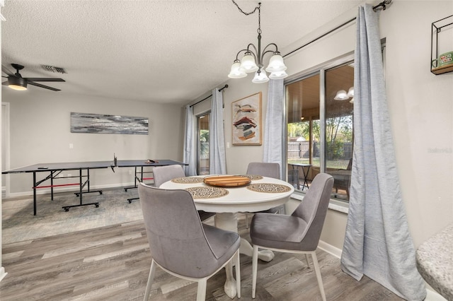 dining area with visible vents, baseboards, ceiling fan with notable chandelier, wood finished floors, and a textured ceiling