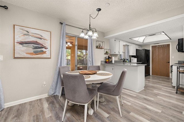 dining space with light wood-style floors, baseboards, and a textured ceiling