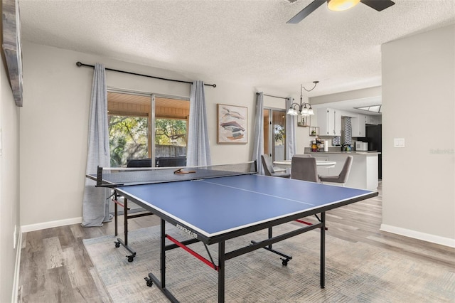 recreation room with light wood-type flooring, baseboards, a textured ceiling, and ceiling fan with notable chandelier