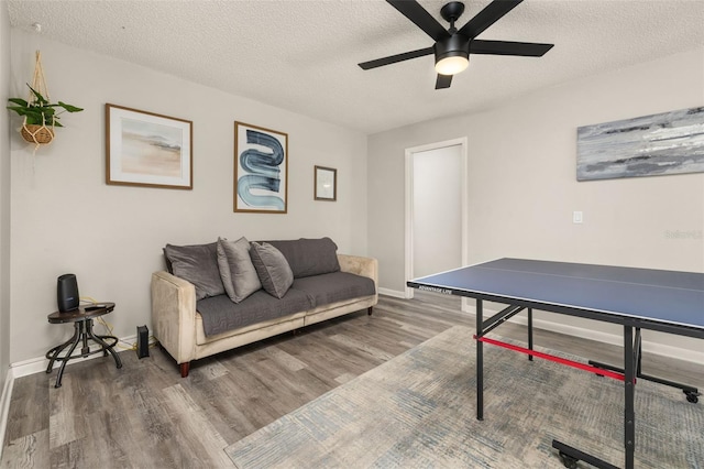 recreation room with baseboards, a textured ceiling, ceiling fan, and wood finished floors