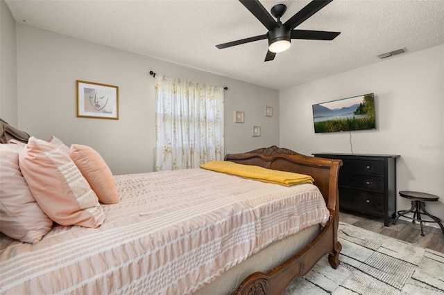 bedroom with visible vents, a textured ceiling, ceiling fan, and wood finished floors