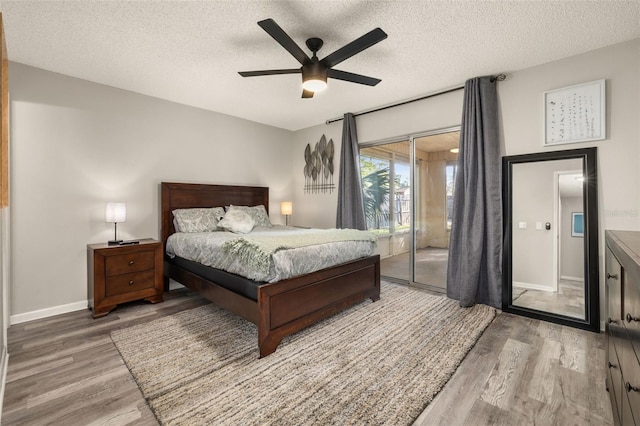 bedroom with access to exterior, a textured ceiling, baseboards, and wood finished floors