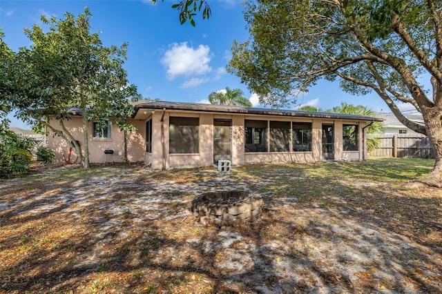 back of property featuring stucco siding, a sunroom, an outdoor fire pit, and fence