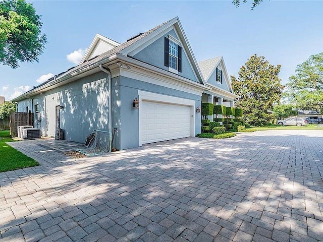 view of home's exterior with central air condition unit, decorative driveway, a garage, and stucco siding