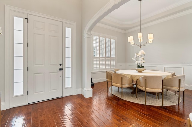 foyer featuring a wainscoted wall, a tray ceiling, arched walkways, dark wood-style flooring, and crown molding