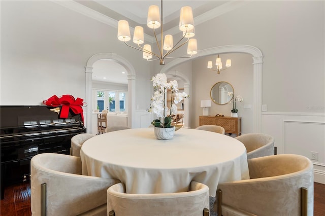 dining room featuring ornamental molding, an inviting chandelier, wainscoting, a decorative wall, and ornate columns