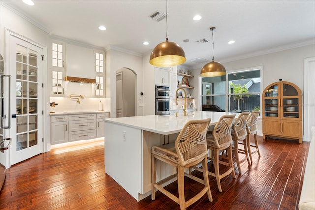 kitchen featuring visible vents, crown molding, light countertops, arched walkways, and dark wood-style flooring