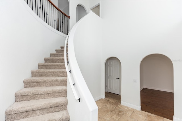 stairs featuring baseboards, arched walkways, a towering ceiling, and stone tile flooring