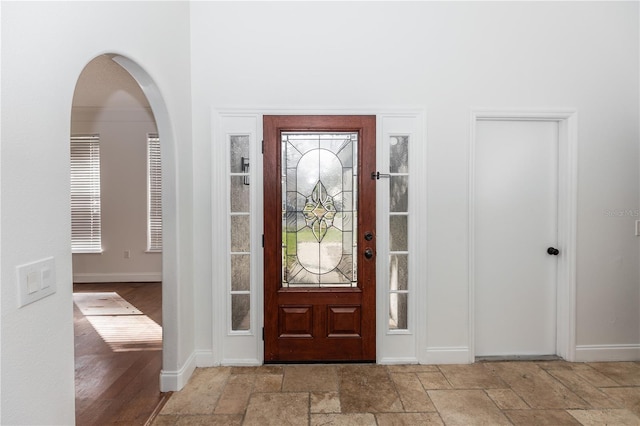 foyer entrance with stone tile floors, arched walkways, and baseboards