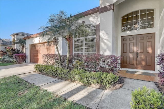 doorway to property featuring an attached garage, driveway, and stucco siding