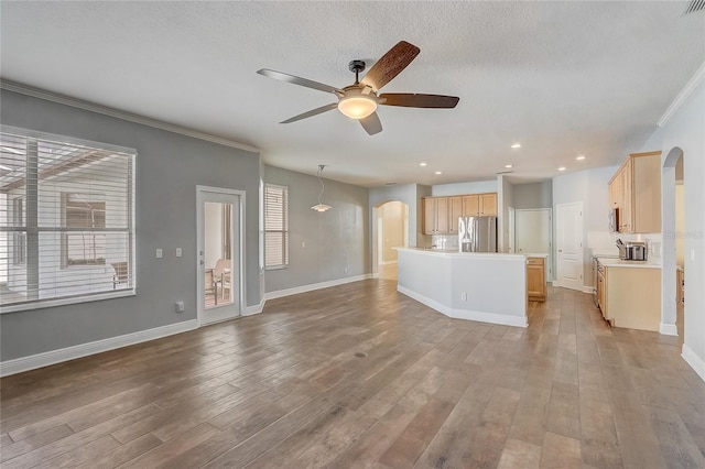 unfurnished living room featuring baseboards, arched walkways, wood finished floors, and a ceiling fan