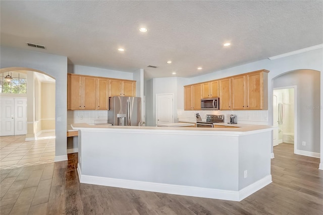 kitchen with wood finished floors, visible vents, arched walkways, and stainless steel appliances