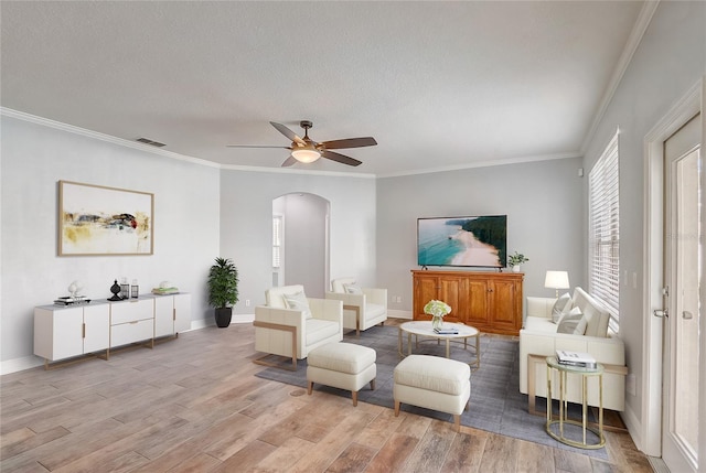 living area with visible vents, light wood-style flooring, ornamental molding, arched walkways, and ceiling fan