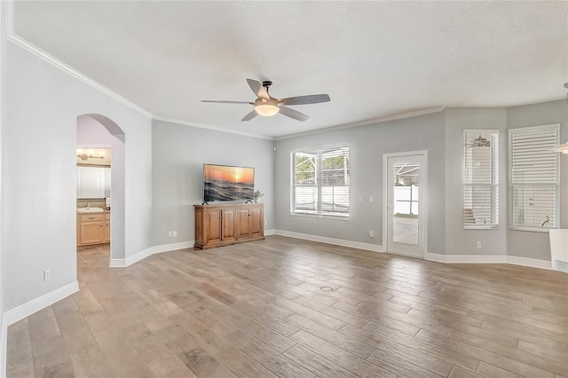 unfurnished living room featuring baseboards, arched walkways, ceiling fan, light wood-style floors, and crown molding