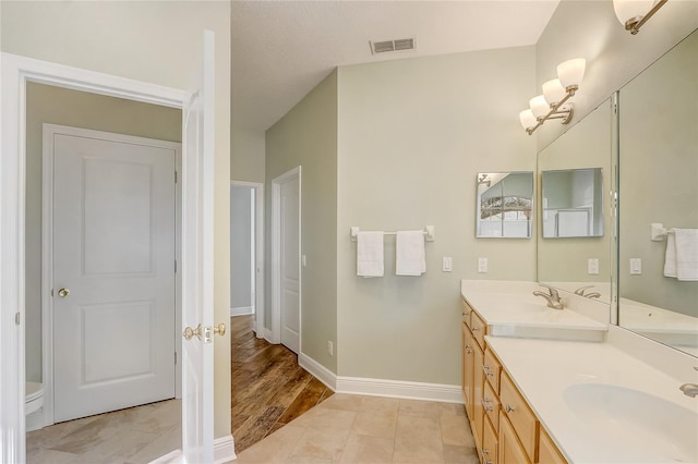 full bath featuring a sink, visible vents, baseboards, and double vanity