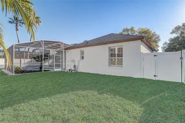 rear view of house with a gate, fence, stucco siding, a lanai, and a lawn