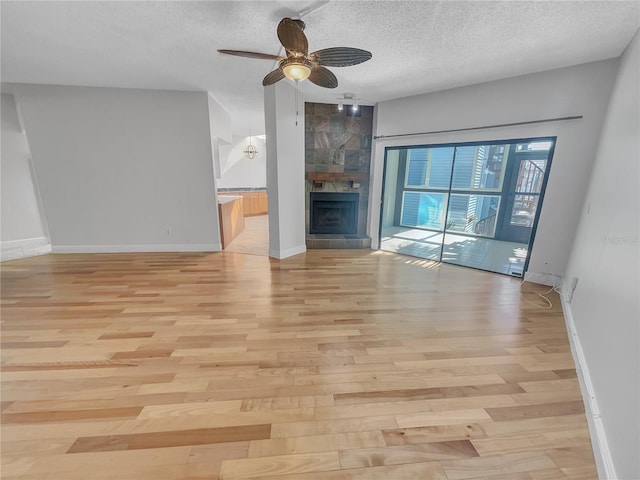 unfurnished living room with baseboards, light wood-style floors, a tiled fireplace, and a textured ceiling