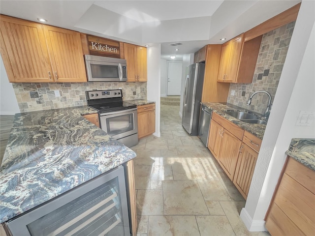 kitchen featuring beverage cooler, dark stone countertops, appliances with stainless steel finishes, and a sink