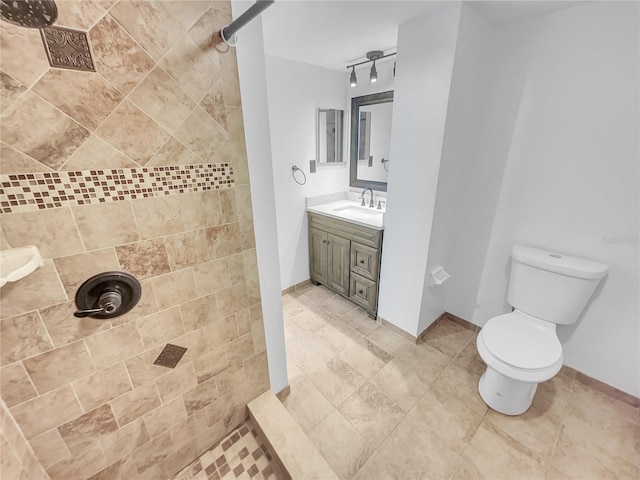 bathroom with a tile shower, toilet, vanity, and baseboards