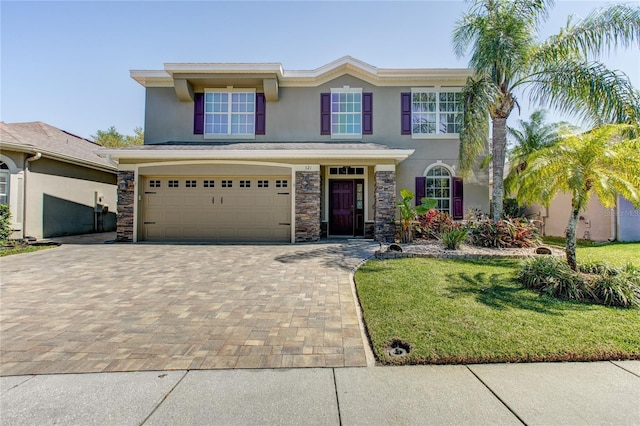 traditional-style home with stucco siding, decorative driveway, stone siding, a front yard, and an attached garage