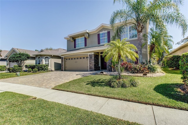 view of front of home featuring a front yard, stucco siding, decorative driveway, stone siding, and an attached garage