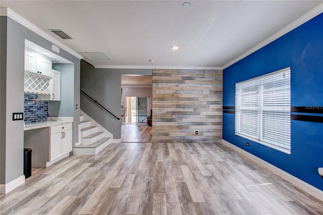 spare room with visible vents, an accent wall, light wood-style floors, crown molding, and stairs