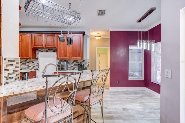 kitchen with visible vents, backsplash, light stone countertops, decorative light fixtures, and light wood-style flooring