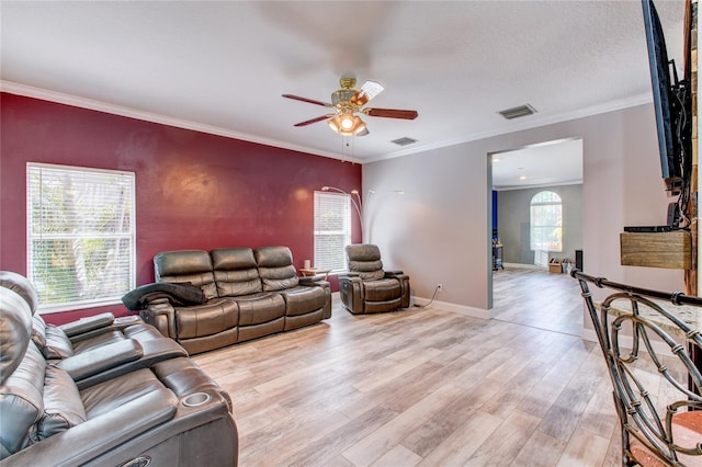 living area with visible vents, ornamental molding, light wood-style floors, baseboards, and ceiling fan