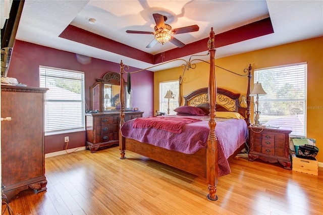 bedroom featuring a tray ceiling, wood finished floors, baseboards, and ceiling fan