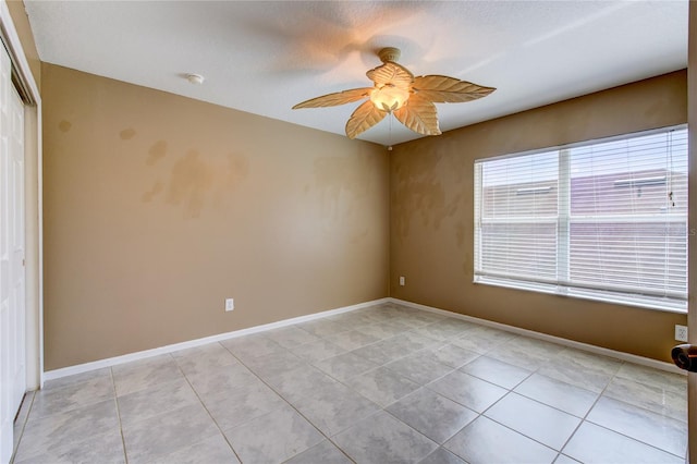 empty room with light tile patterned floors, a ceiling fan, and baseboards