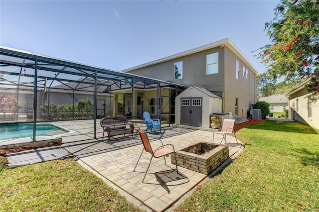 rear view of house with glass enclosure, an outdoor fire pit, a yard, a storage shed, and central air condition unit