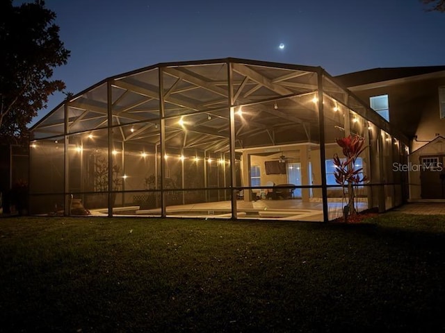 back of house at twilight featuring a lanai, a patio area, and a lawn