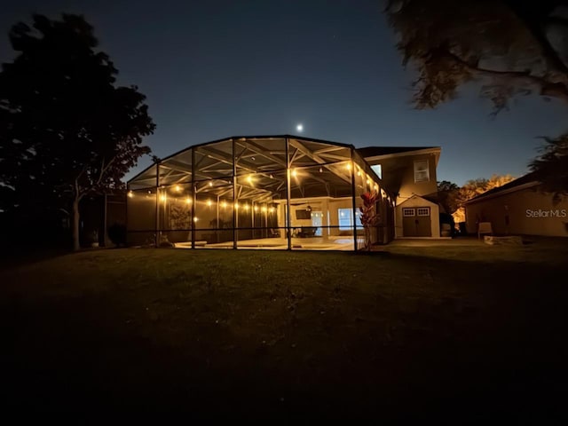 back of house at twilight with glass enclosure, a storage shed, and an outdoor structure