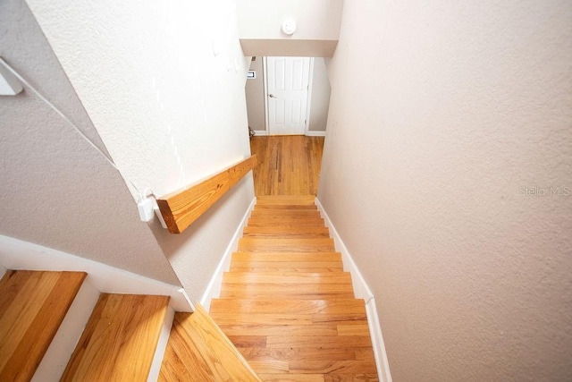 stairway with wood finished floors, baseboards, and a textured wall