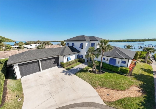 traditional-style home featuring a front lawn, a water view, stucco siding, driveway, and an attached garage