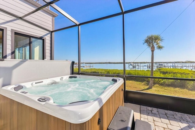 view of patio / terrace with a lanai, a hot tub, and a water view