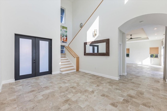 foyer with baseboards, a high ceiling, arched walkways, ceiling fan, and stairs